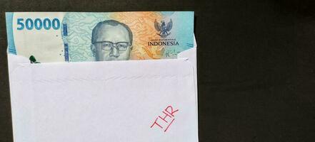 A white envelope written of THR and new Indonesian banknotes, usually Tunjangan Hari Raya or called THR are given to employees ahead of Eid. photo