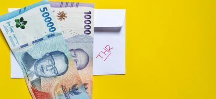 A white envelope written of THR and new Indonesian banknotes, usually Tunjangan Hari Raya or called THR are given to employees ahead of Eid. Negative space photo