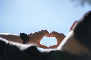 Male hands in the shape of a heart on the sky as background. photo