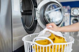 Woman picking up dirty clothes in a bin and putting them in the washing machine in a laundry shop photo