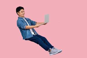 Young asian businessman holding laptop computer floating in the air isolated on pink background photo