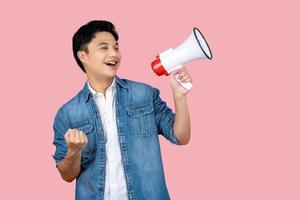 Announcement. Happy asian man shouting loud at megaphone, recruiting, protesting with speaker in hands, standing over pink background photo