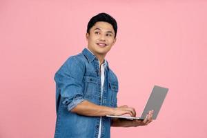 Young Asian business man using laptop computer and looking at camera isolated on pink background photo