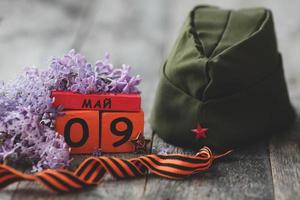 Wooden calendar with Russian text May 9, garrison cap, george ribbon and a bouquet of lilacs . Victory Day. photo