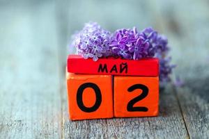 Wooden calendar with Russian text May 2 and a bouquet of lilacs on a wooden background. Copy space. photo