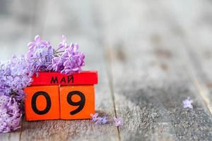 Wooden calendar with Russian text May 9 and a bouquet of lilacs on a wooden background. Victory Day. Copy space. photo