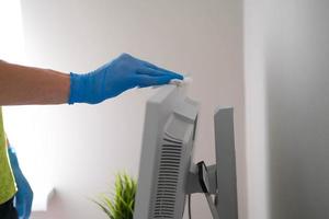 un masculino mano en caucho guantes toallitas el polvo desde un computadora monitor con un servilleta. desinfección a hogar, limpieza en el contexto de el covid-19 pandemia. foto