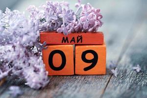 Wooden calendar with Russian text May 9,  george ribbon and a bouquet of lilacs on a wooden background. Victory Day. photo