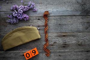 Flask, george ribbon, garrison cap and lilacs on a wooden background. Wooden calendar with date 9 May. Victory Day. Copy space. photo