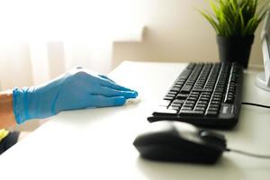 Male hands in rubber gloves wipe the white table and keyboard from the computer. Disinfection in the office during the COVID-19 photo