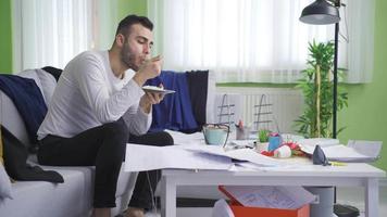 paresseux homme est content et en mangeant le sien repas dans le sien désordonné maison. une Jeune homme avec une désordonné maison est contenu et détendu avec pollution. video