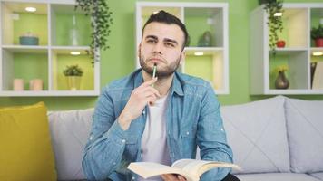 Happy and smiling young man reading a book at home daydreaming. Young man reading books dreams, attaches importance to interesting information. video