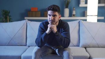 depressivo e ansioso homem pensando às lar. jovem homem sentado às casa infeliz e entediado, pensativo preocupações sobre a futuro, triste, sozinho. video