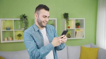 content et détendu Jeune homme en utilisant téléphone à maison. content et souriant Jeune homme navigation le téléphone à maison. video