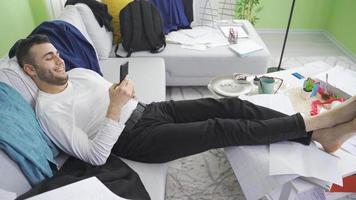 Relaxed lazy man uses phone in his dirty and untidy home.  The man with a reckless lifestyle is lazy and disorganized. video