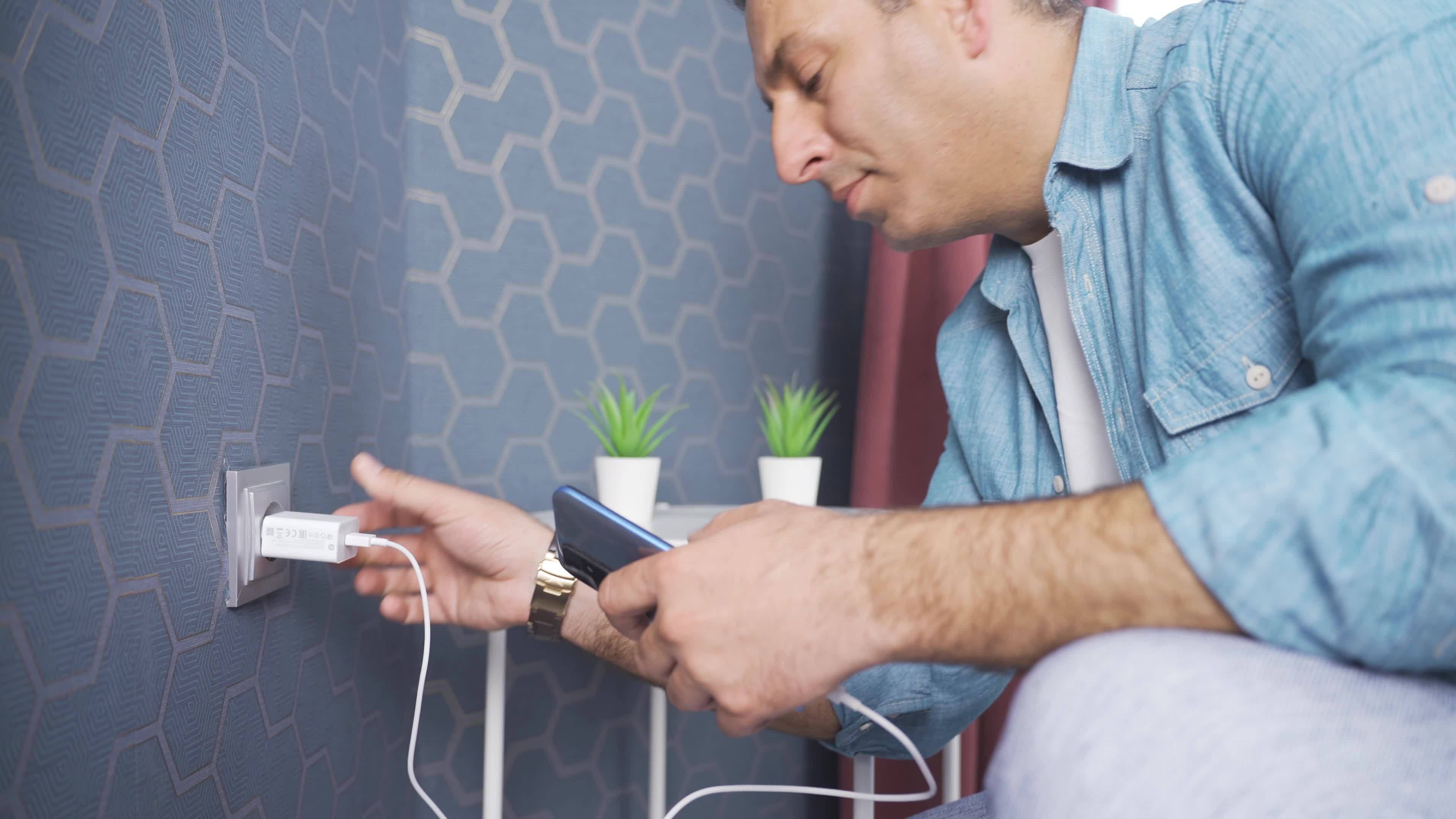 Man plugging mobile phone charger into wall power outlet. The man who