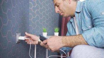 Man plugging mobile phone charger into wall power outlet. The man who plugs in the power plug charges his phone. Power saving or cost reduction concept. video