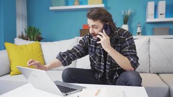 casa escritório trabalhador fazer uma telefone ligar com dele cliente. o negócio pessoa falando em a telefone às lar. ele é dizendo alguma coisa enquanto olhando às a computador portátil. video