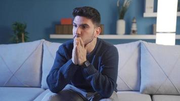 jovem homem com ansiedade transtorno é considerado. jovem homem sentado em sofá às casa às noite é considerado, nervoso, tem preocupações. video