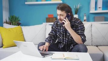 homem trabalhando dentro casa escritório. casa escritório trabalhador homem falando em a telefone e levando notas. ele é olhando às a computador portátil. video