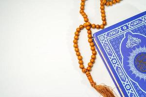 The Holy Al Quran with written arabic calligraphy meaning of Al Quran and rosary beads or tasbih on white background with copy space. photo