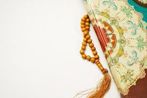 The Holy Al Quran with written arabic calligraphy meaning of Al Quran and rosary beads or tasbih on white background with copy space. photo