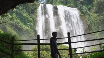 Silhouette man walking in front of the cave and water fall. The photo is suitable to use for adventure content media, nature poster and forest background. video