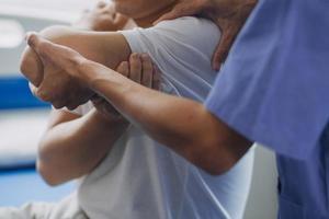 médico o fisioterapeuta trabajando examinando tratando lesionado brazo de atleta masculino paciente, extensión y ejercicio, haciendo el rehabilitación terapia dolor en clínica. foto