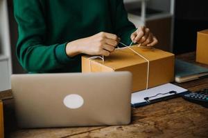 SME entrepreneur Small business entrepreneurs Online selling ideas,Happy Young Asian business owner work on computer and a boxs at home,delivery SME procurement package box deliver to customers, photo