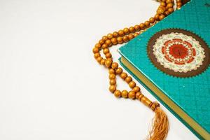 The Holy Al Quran with written arabic calligraphy meaning of Al Quran and rosary beads or tasbih on white background with copy space. photo