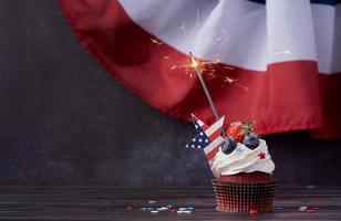 Sweet cupcake with blueberries and strawberry and sparkler over USA flag background photo