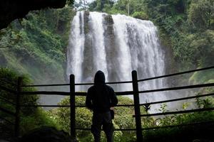 Silhouette man on the cave in front of great water fall, Semarang Central Java. The photo is suitable to use for adventure content media, nature poster and forest background.