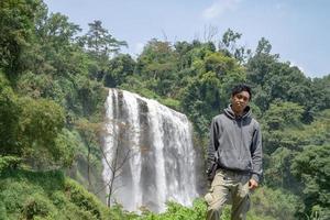 Man stand wear hoody in front of the great water fall with hand reel, Semarang central Java. The photo is suitable to use for adventure content media, nature poster and forest background.