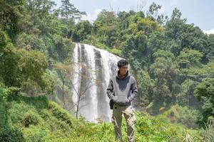 Man stand wear hoody in front of the great water fall with hand reel, Semarang central Java. The photo is suitable to use for adventure content media, nature poster and forest background.