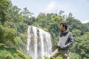 Man stand wear hoody in front of the great water fall with hand reel, Semarang central Java. The photo is suitable to use for adventure content media, nature poster and forest background.