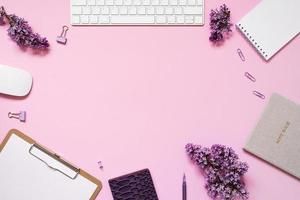 Keyboard and mouse, notebooks, pen, a bouquet of lilacs on a pink background. Purple spring flowers. Composition for a blogger. Copy space photo