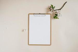 Blank sheet of paper with clipboard for tablet with copy space for copy. Beautiful home office table table workspace with fresh apple tree flowers. Flat lay, top view art concept photo