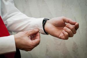 Man fastens a button on the sleeve of a white shirt in close-up photo