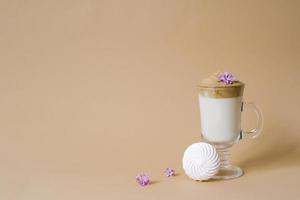 Beautiful dalgon coffee drink with foam in a transparent Cup and marshmallows on a beige background. Copy space photo