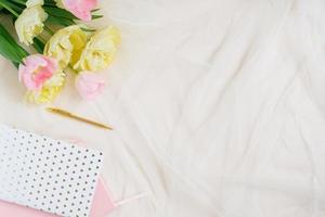 Notepads with pen and pink yellow tulips on beige desk background. Template for advertising or visualization of blog with copy space, text place. Certificate mockup. Top view. Business holiday card. photo