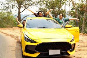 Middle-aged Asian woman and friends with a lover's yellow sedan. Everyone smiled happily. to travel the mountains on a summer vacation together.soft and selective focus. photo