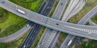 Aerial top view of highway junction interchange road. Drone view of the elevated road, traffic junctions, and green garden. Transport trucks and cars driving on highway. Infrastructure in modern city. photo