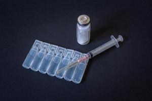 A vial of powder, a disposable syringe and a vaccine in ampoules are on a black background. Transparent liquid in plastic ampoules. Vignetting. Horizontal. photo