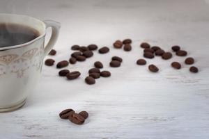 A cup of coffee with steam on a white background in paint and coffee beans are nearby. Selective focus on the first coffee beans, others blurred. Place for text. photo