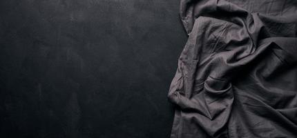 Folded black linen linen kitchen towel on a black background, top view. Copy space photo