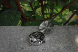 Concept for nature and adventure. After some edits, a photo of a compass placed outdoor near a tree.