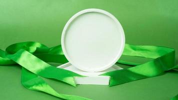 White round podium with green satin ribbon on a green background. Free space for text. April Green Month of awareness about the importance of safety at work photo