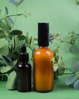 Glass bottles of toner and serum with leaves on green background. Beauty product packaging display photo