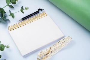 Notebook with pen and measuring tape on white background, diet and healthy living concept photo