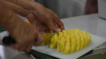 The cook hand with sharp knife slicing delicious pineapple on the white chopping board. video